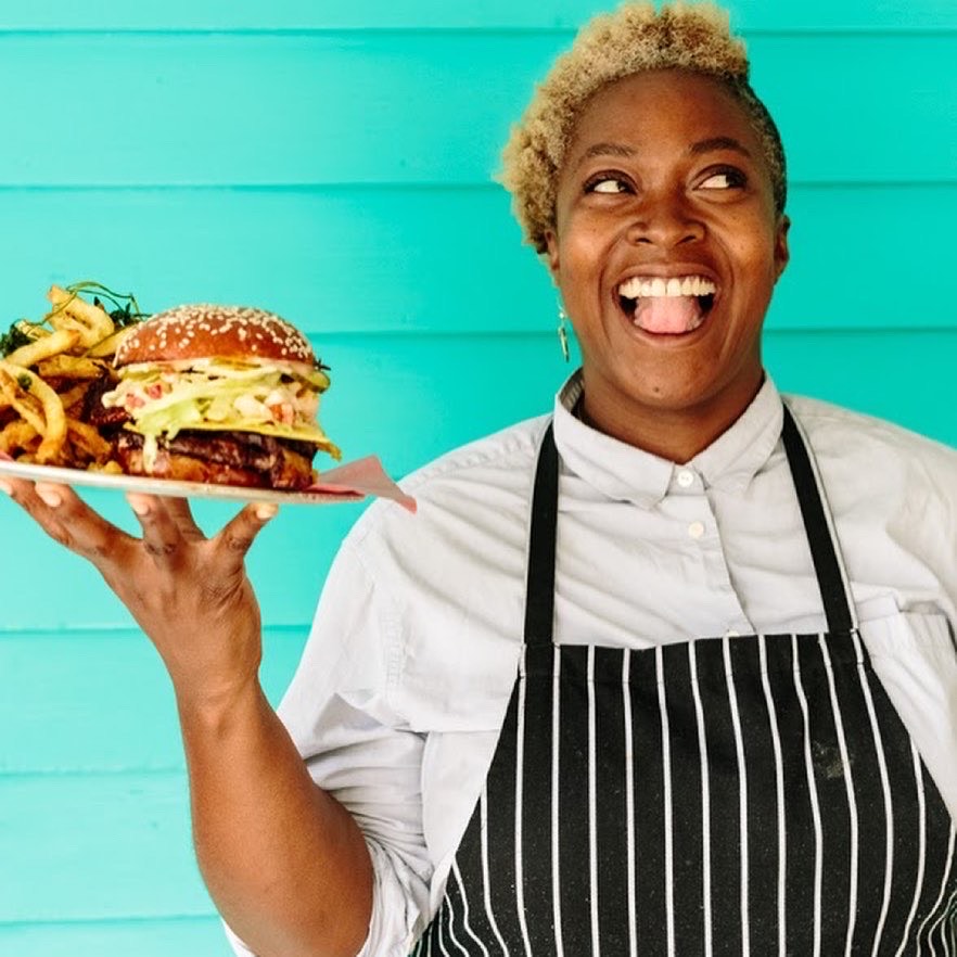 smiling woman holding up a tray with burger and fries against a bright teal background