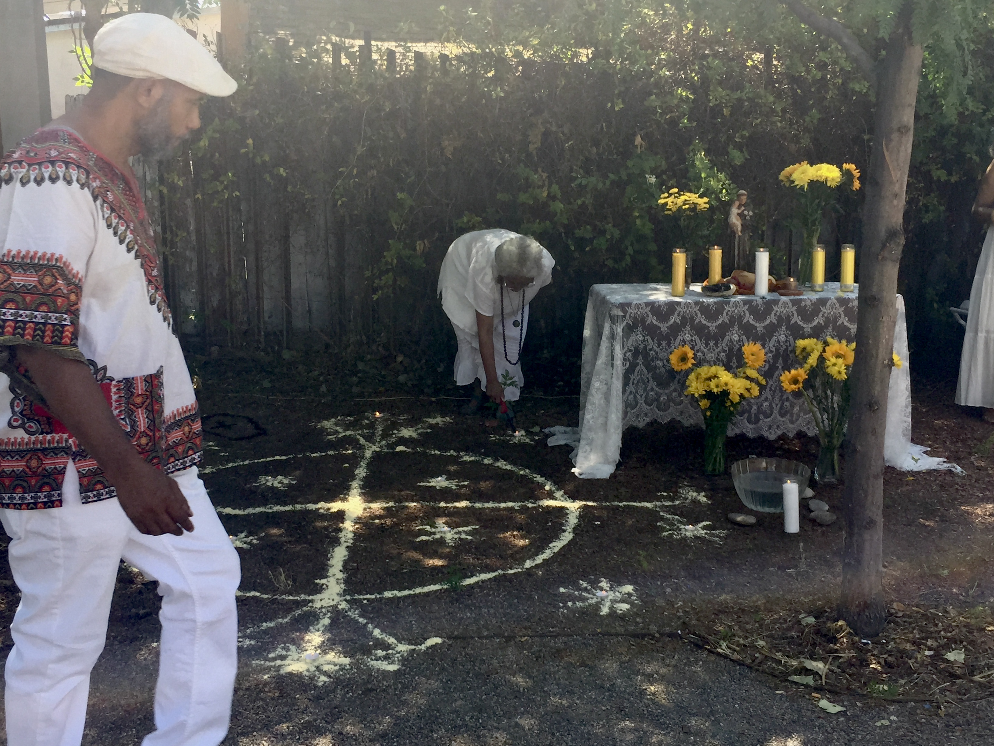 Two People dressed in white at Papa Legba event, altar, yellow flowers